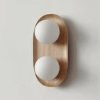 Front view of this Clérachic wall light in natural wood, two frosted globes on an oval frame, against a pale grey wall.