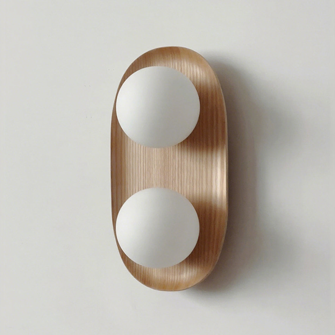 Front view of this Clérachic wall light in natural wood, two frosted globes on an oval frame, against a pale grey wall.