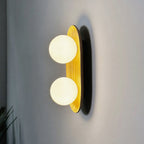 Closer view of the lit Clérachic wall light, two warm-white globes on a golden wood oval with a dark shadow on the wall.