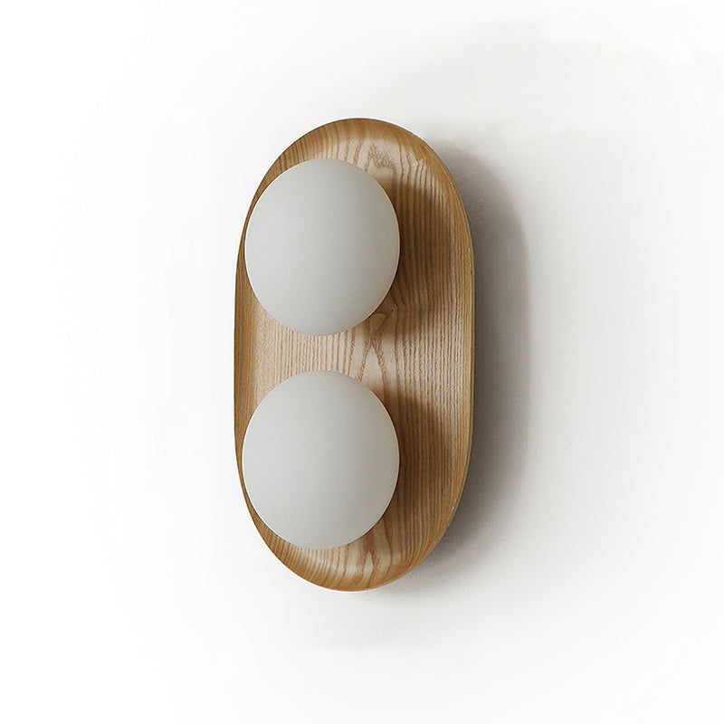 Studio view of this Clérachic wall light in a light wood finish, two frosted globes on a soft-edged oval frame.