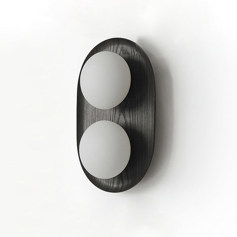 Studio view of this Clérachic wall light in black, two frosted globes on an oval frame with a fine wood-grain texture.