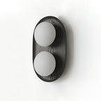 Studio view of this Clérachic wall light in black, two frosted globes on an oval frame with a fine wood-grain texture.
