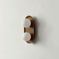 The smaller Clérachic wall light in a wood finish, two frosted globes on a slim oval frame, shown on a pale wall.
