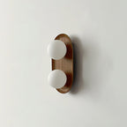 The smaller Clérachic wall light in a wood finish, two frosted globes on a slim oval frame, shown on a pale wall.