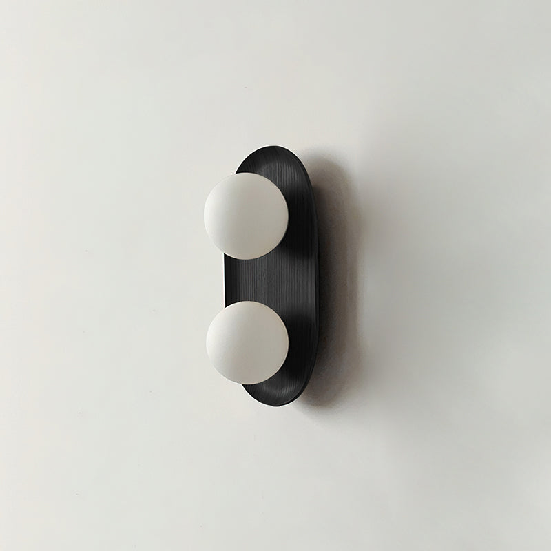 The smaller Clérachic wall light in black, with two frosted globes on a slim oval frame and a soft shadow on a pale wall.