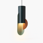 Clérachic teal metal cylinder pendant lit warm, its sage oval and terracotta half-disc glowing from the downlight.