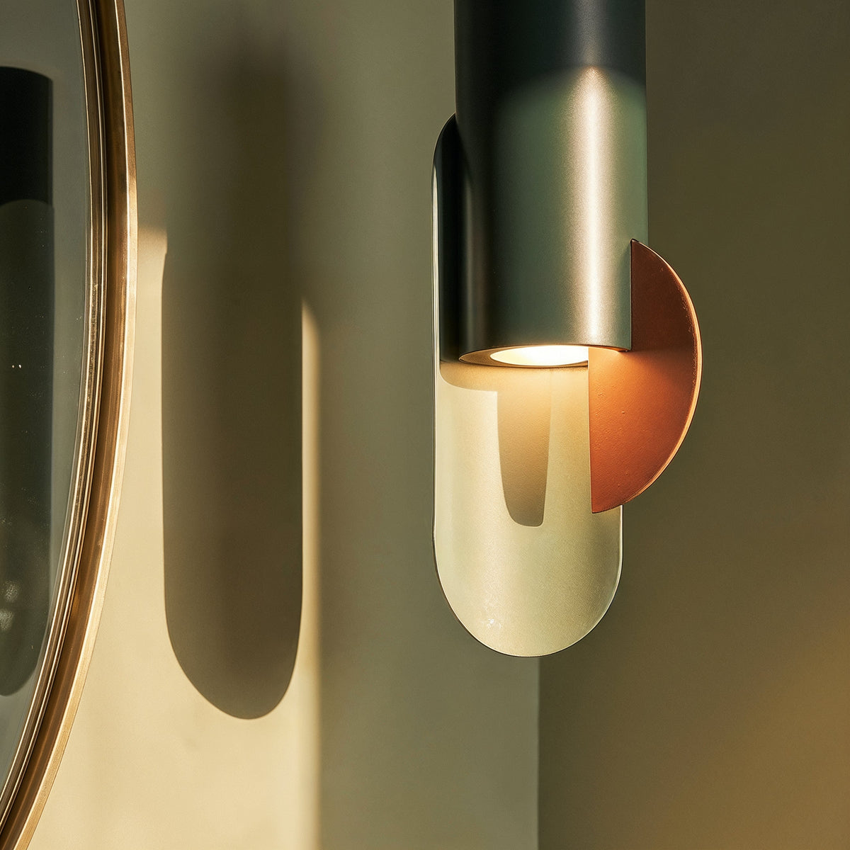 Close view of a Clérachic cylinder pendant, its warm downlight washing a pale oval plate and a copper-toned half-disc.