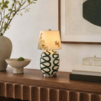 Clérachic table lamp with a cream base painted in dark green loops, on a ribbed wood console with a stone bowl and stacked books.