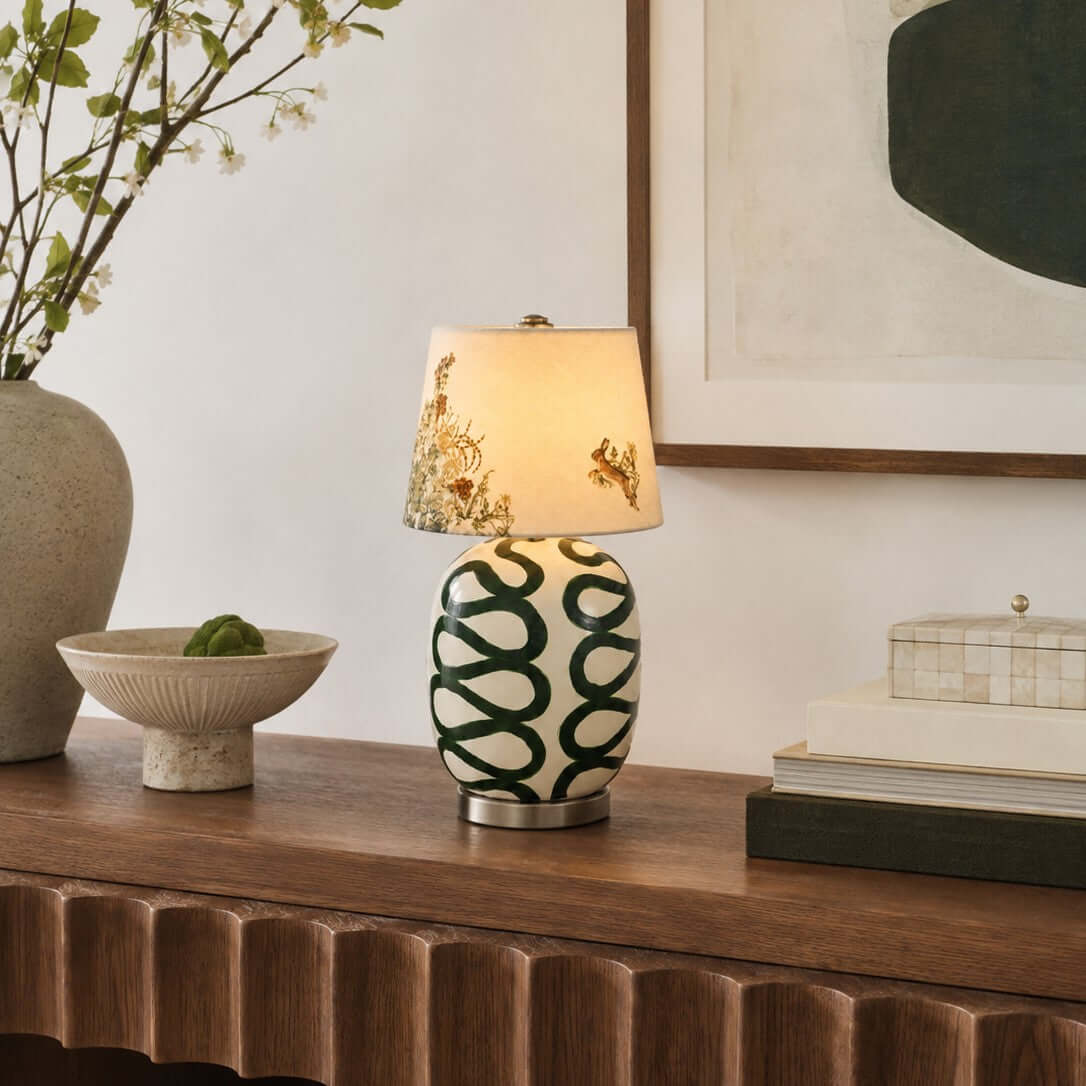 Clérachic table lamp with a cream base painted in dark green loops, on a ribbed wood console with a stone bowl and stacked books.