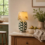 Lit Clérachic table lamp with green looped glaze on a rattan-drawered cabinet, with a bowl of pears and a linen cloth.