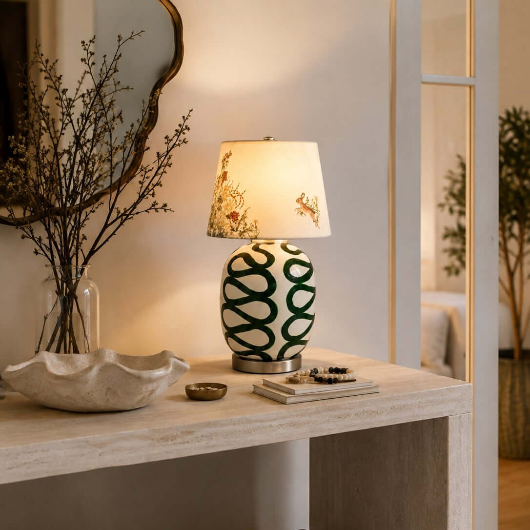 Warm light from this Clérachic table lamp with a green looped base, on a pale console with a shell-shaped dish and a mirror behind.