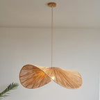 This Clérachic pendant hangs lit on a long cord, a palm leaf edging into the plain backdrop.