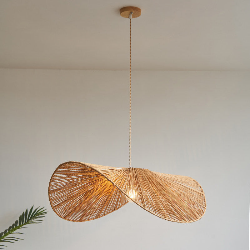 This Clérachic pendant hangs lit on a long cord, a palm leaf edging into the plain backdrop.