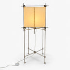 A Clérachic floor lamp with a square parchment shade on a slim metal frame with cross-braced legs and a foot switch, on white.