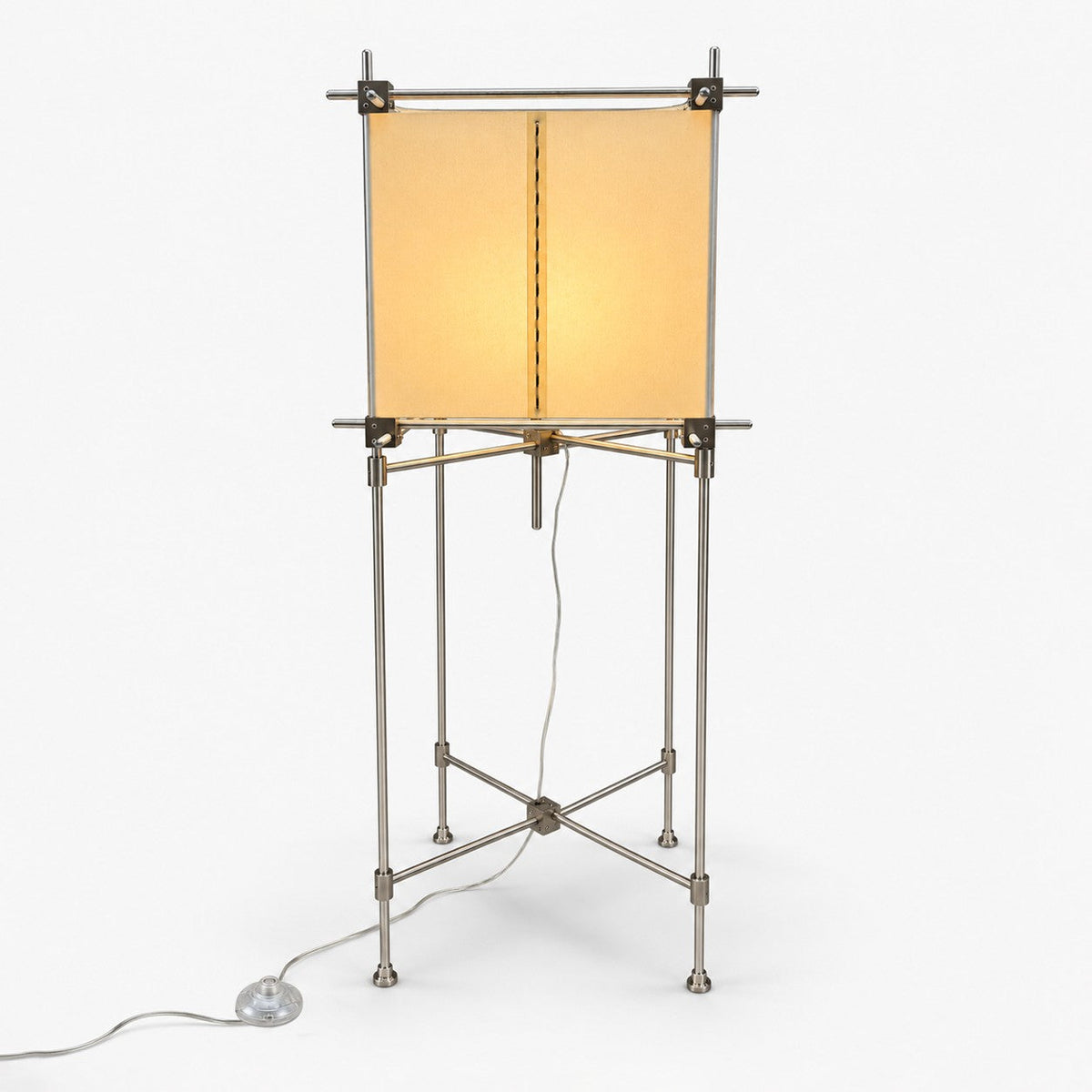 A Clérachic floor lamp with a square parchment shade on a slim metal frame with cross-braced legs and a foot switch, on white.