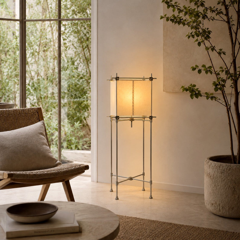 A Clérachic floor lamp with a parchment cube shade stands near a glass wall, with a large planter and a rattan chair at its side.