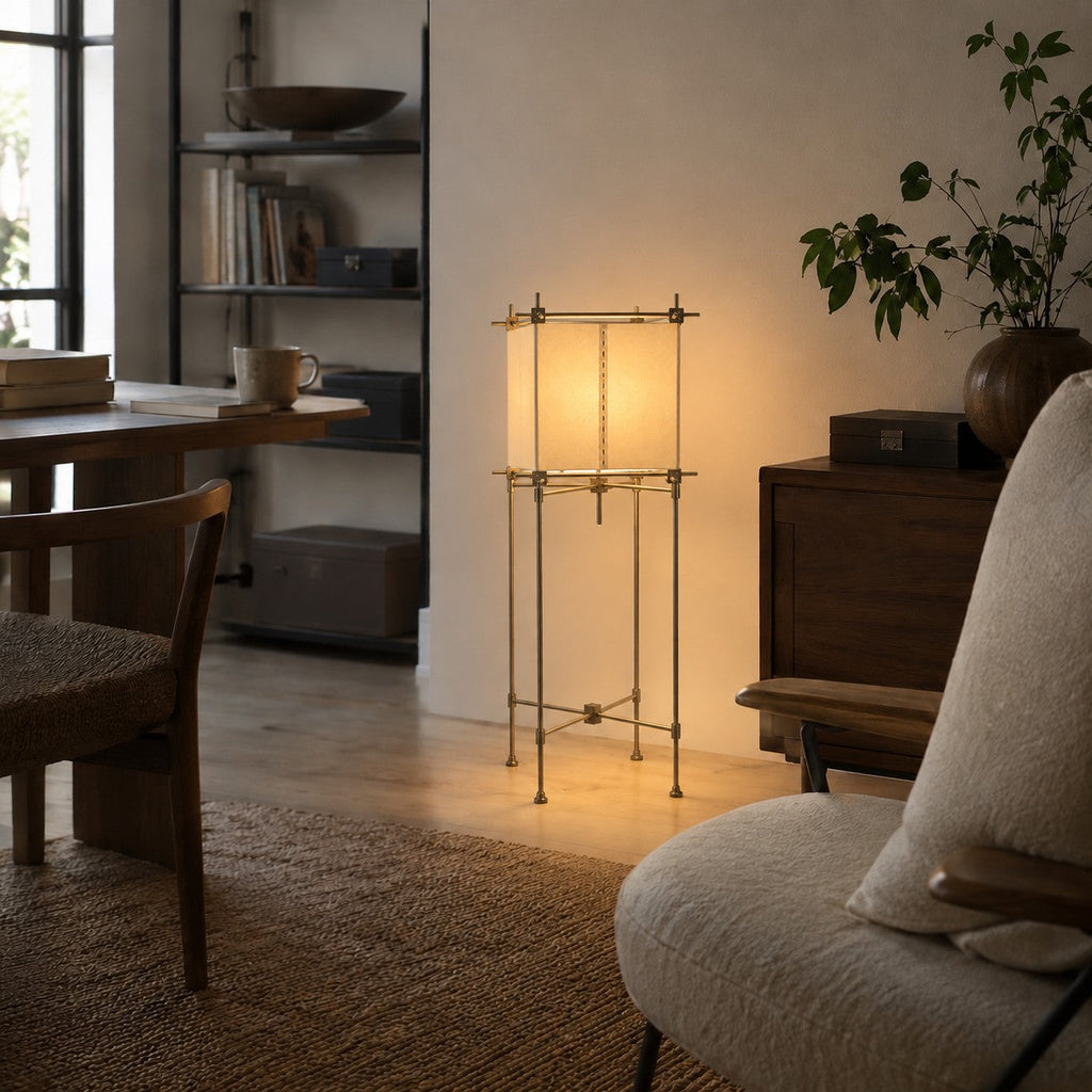 Clérachic paper cube floor lamp lit between a dark wood sideboard and a work desk, with a bookshelf behind and a cushioned chair.