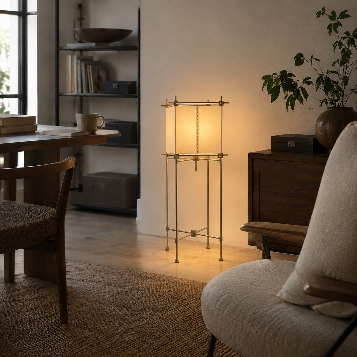 Clérachic paper cube floor lamp lit between a dark wood sideboard and a work desk, with a bookshelf behind and a cushioned chair.