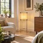 This Clérachic floor lamp stands in a living room corner beside a walnut chest of drawers and a cream armchair with a striped cushion.