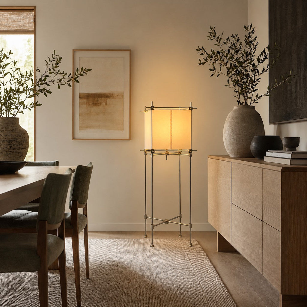 A Clérachic parchment cube lamp on a slim metal stand, beside a pale oak sideboard and a large vase of olive branches.