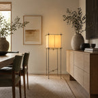 A Clérachic parchment cube lamp on a slim metal stand, beside a pale oak sideboard and a large vase of olive branches.