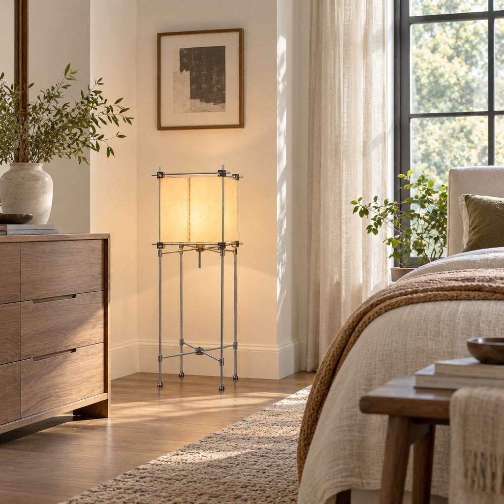 Clérachic floor lamp with a cube shade between a wooden chest of drawers and the corner of a bed with a brown throw.