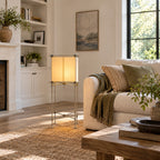 This Clérachic cube floor lamp stands before built-in white shelves, with a cream sofa and a rustic wood coffee table in sunlight.
