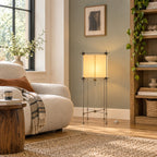 Clérachic floor lamp with a glowing paper cube shade against a sage wall, beside a wooden bookcase and a boucle sofa.