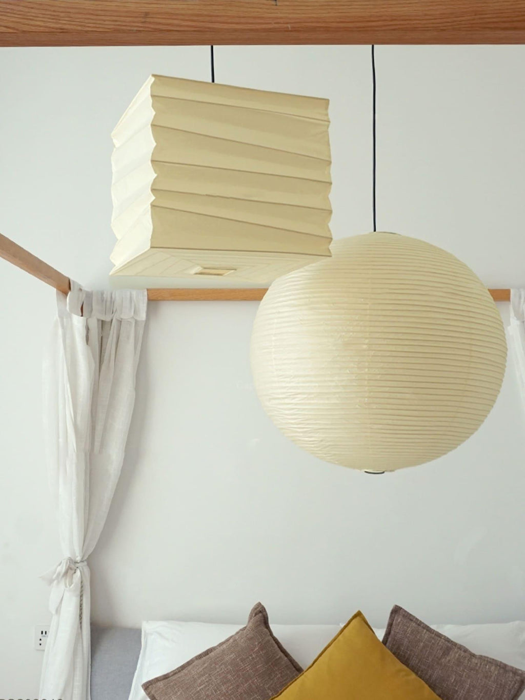 Clérachic paper cube pendant light set unlit on a wooden ledge beside a large round paper lantern, sheer white curtains tied back below.