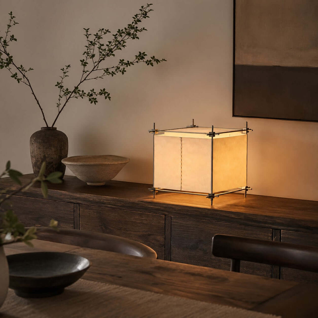 On a dark wooden console with a branch in a vase, this Clérachic cube lamp shows its parchment panels lit from within.