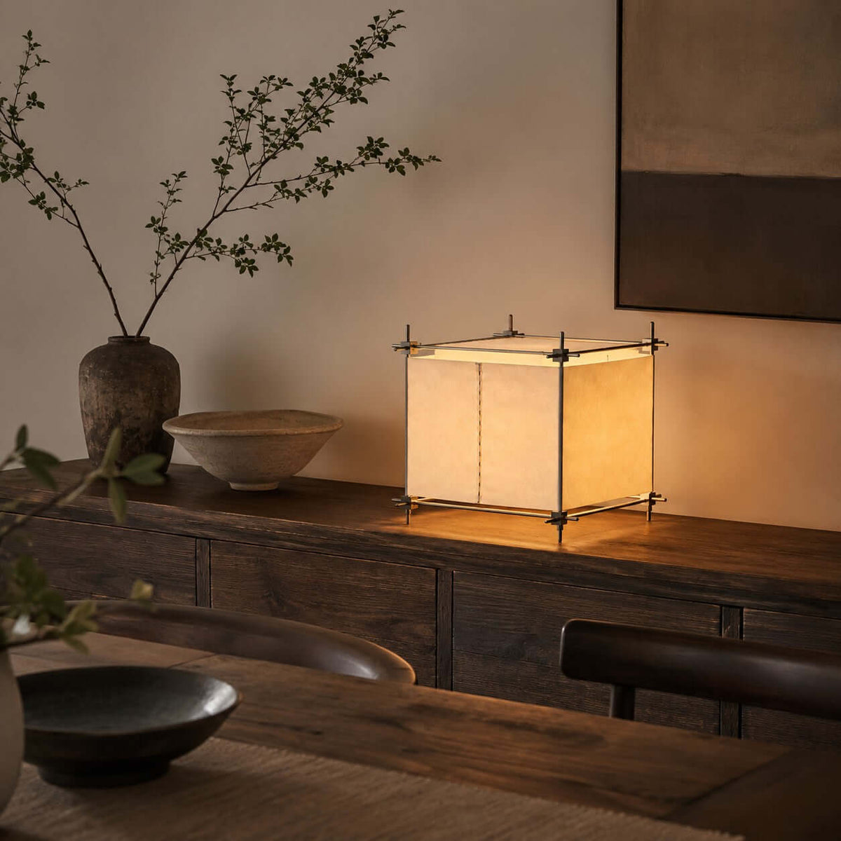 On a dark wooden console with a branch in a vase, this Clérachic cube lamp shows its parchment panels lit from within.