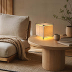 Next to a low round oak coffee table and a linen armchair, this Clérachic cube lamp glows in a corner of a calm sitting room.