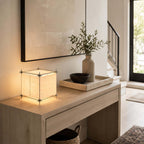 On a pale console with a drawer and a tray of small bowls, this Clérachic cube lamp lights the wall beside a large framed canvas.