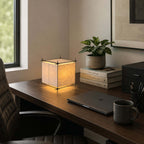 On a dark walnut desk with a laptop, books and a mug, this Clérachic cube lamp gives a warm glow beside a potted plant.