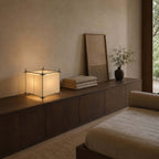 Low on a long walnut sideboard with folded towels and a framed print, this Clérachic cube lamp gives a soft evening light.