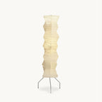 Tall folded washi paper floor lamp from Clérachic on a white backdrop, with a pale shade on three thin black iron legs.