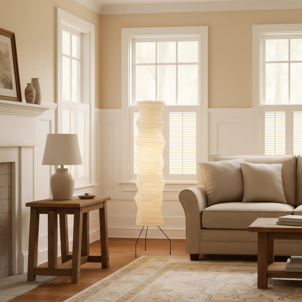 Clérachic tall paper floor lamp lit in a panelled living room with a wooden side table, a table lamp and a beige sofa.