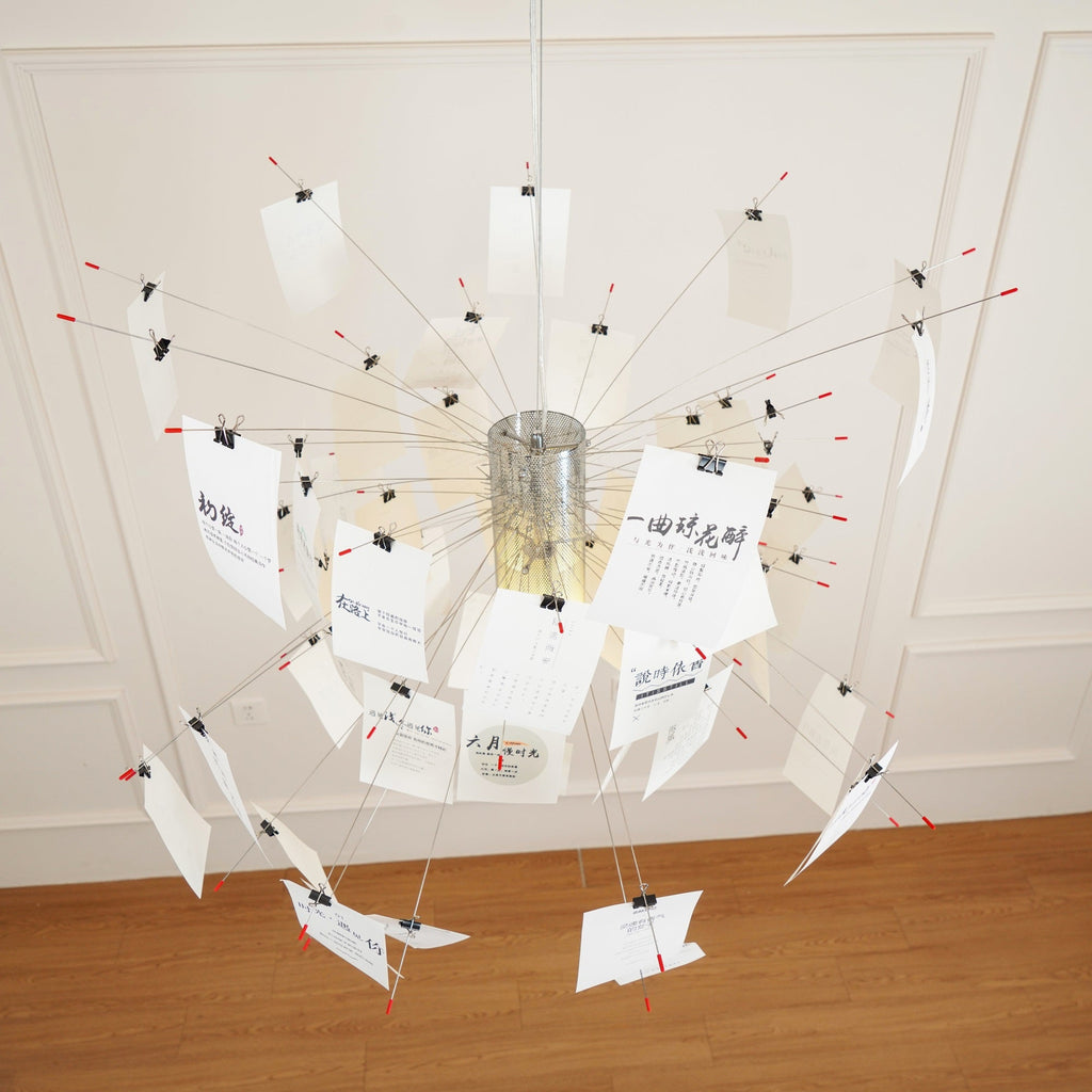 Seen from below, the metal core and red-tipped wire arms of this Clérachic pendant carry cards printed with calligraphic text.