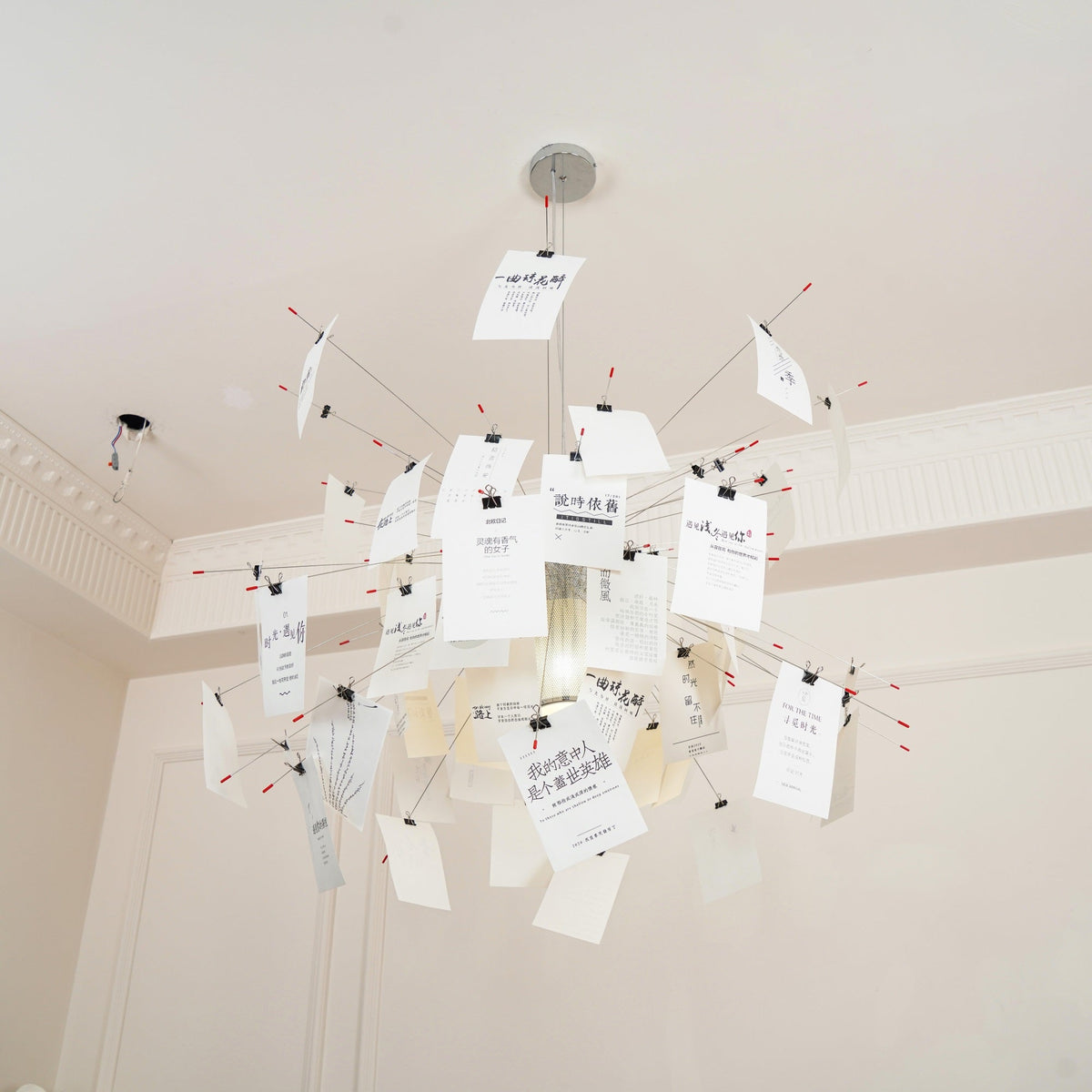 Under a cornice and a high plaster ceiling, this Clérachic paper pendant fans out cards on thin wire arms around a glowing core.