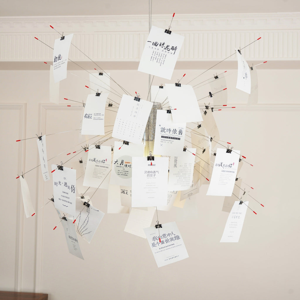 Close view of a Clérachic paper pendant with printed text cards clipped to red-tipped wire arms against a panelled wall.