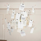 Close view of a Clérachic paper pendant with printed text cards clipped to red-tipped wire arms against a panelled wall.