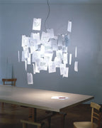 A Clérachic paper pendant above a long table in a grey-blue room, with handwritten notes clipped all over its frame.