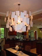 Over a dining table with a candle, this Clérachic paper pendant lights a kitchen with its stacked white note cards.