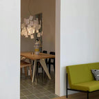 Seen through a doorway, a Clérachic paper pendant hangs above a pale wood table and a lime-green sofa.
