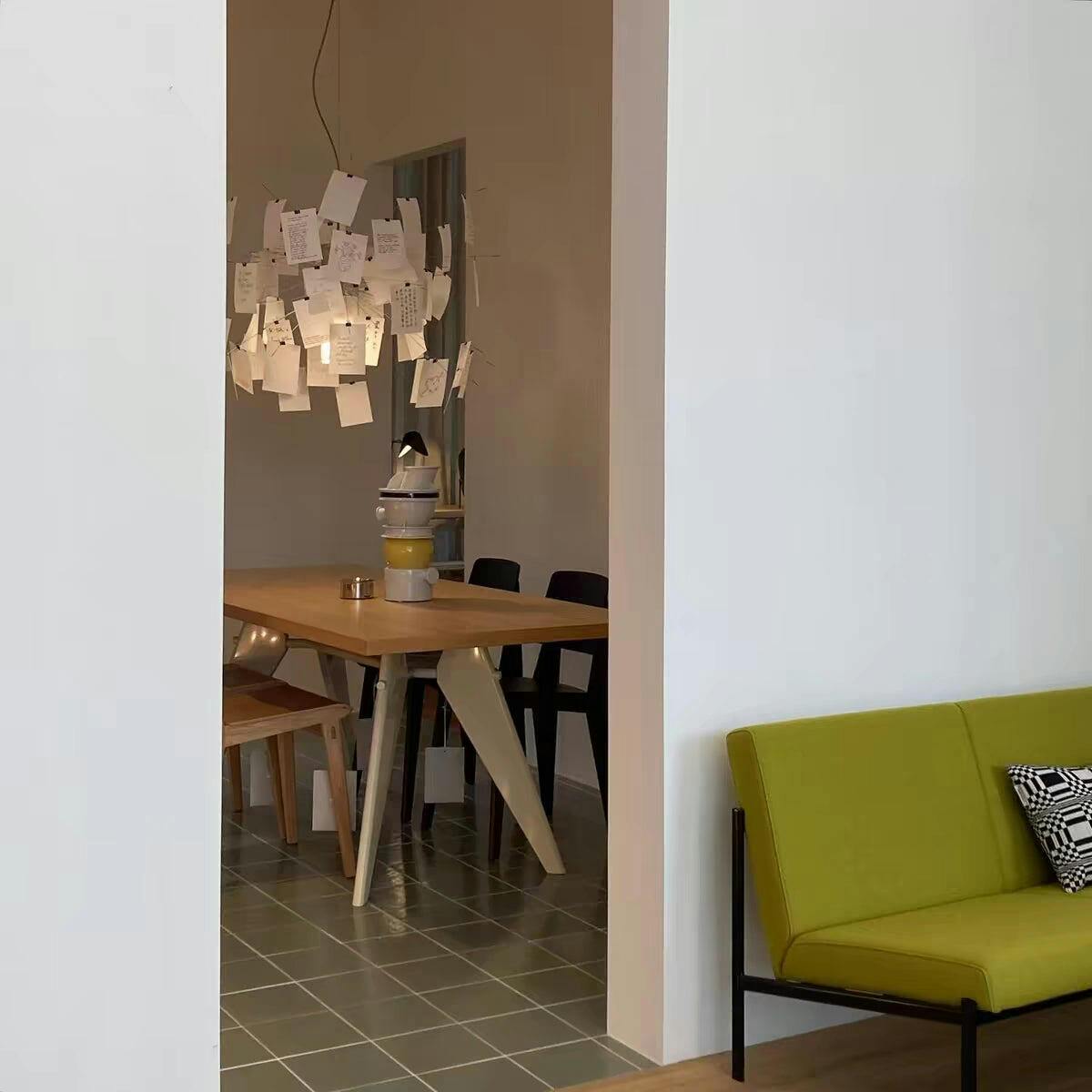 Seen through a doorway, a Clérachic paper pendant hangs above a pale wood table and a lime-green sofa.