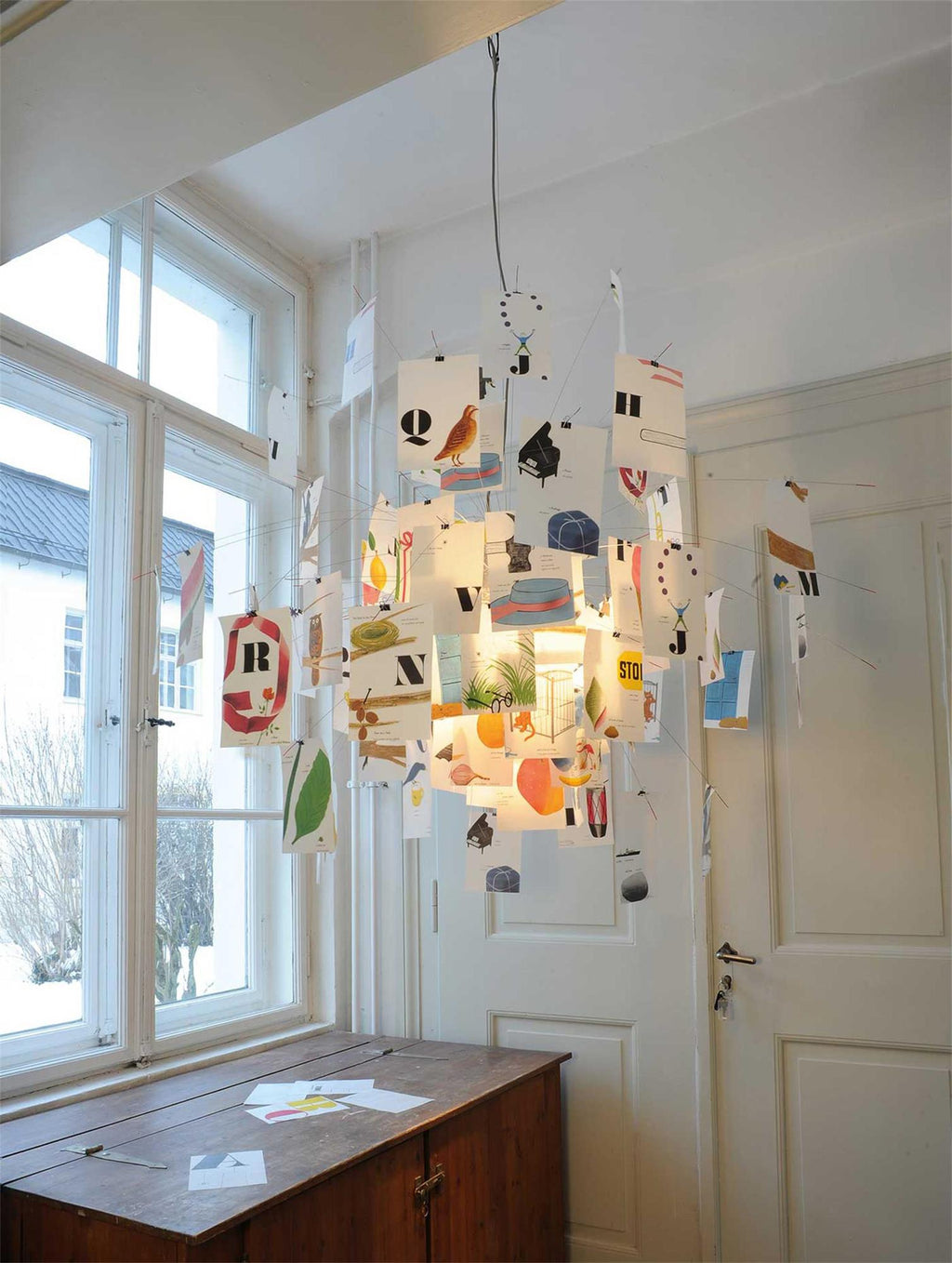 This Clérachic paper pendant is lit up by tall windows, its printed alphabet cards glowing warm against a white door.