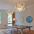 Two Clérachic paper pendants hang over a large dark dining table in a room with ghost chairs and round wall art.