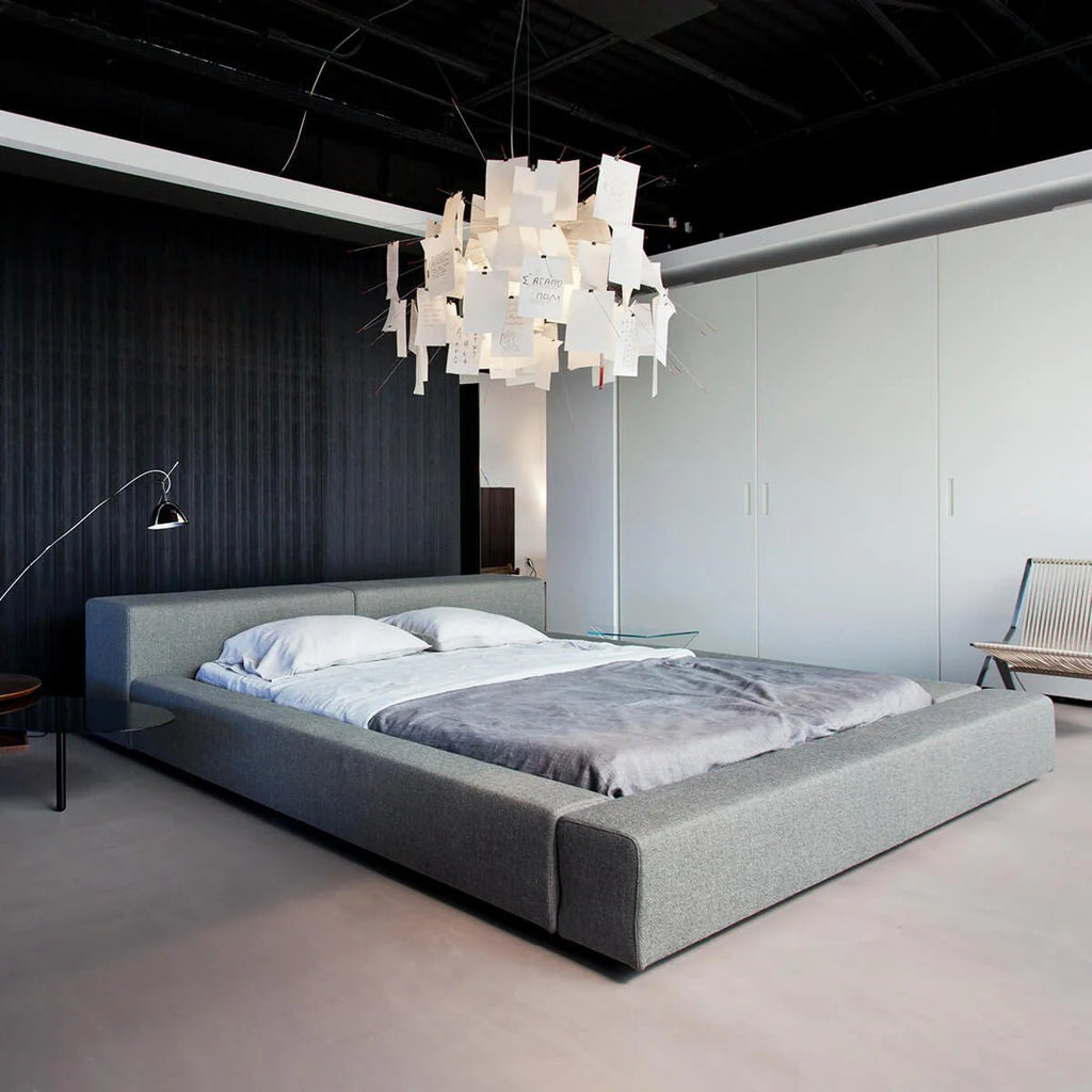Above a low grey bed in a dark-panelled bedroom, a Clérachic paper pendant fills the ceiling with white notes.