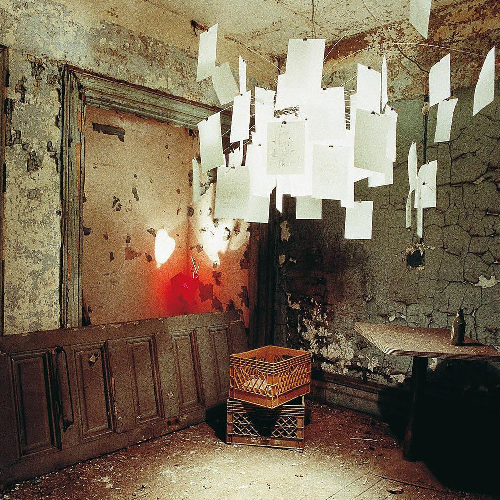 A Clérachic paper pendant hangs in a weathered, peeling room, its white paper notes glowing against the old walls.