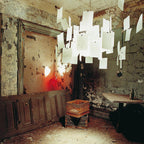 A Clérachic paper pendant hangs in a weathered, peeling room, its white paper notes glowing against the old walls.